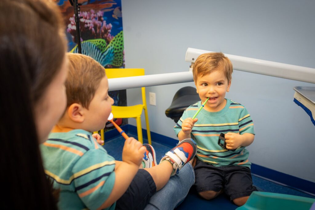 Infant Dental Exams 1 Two Toddlers Holding Toothbrushes With Their Mom At Cobblestone Kids